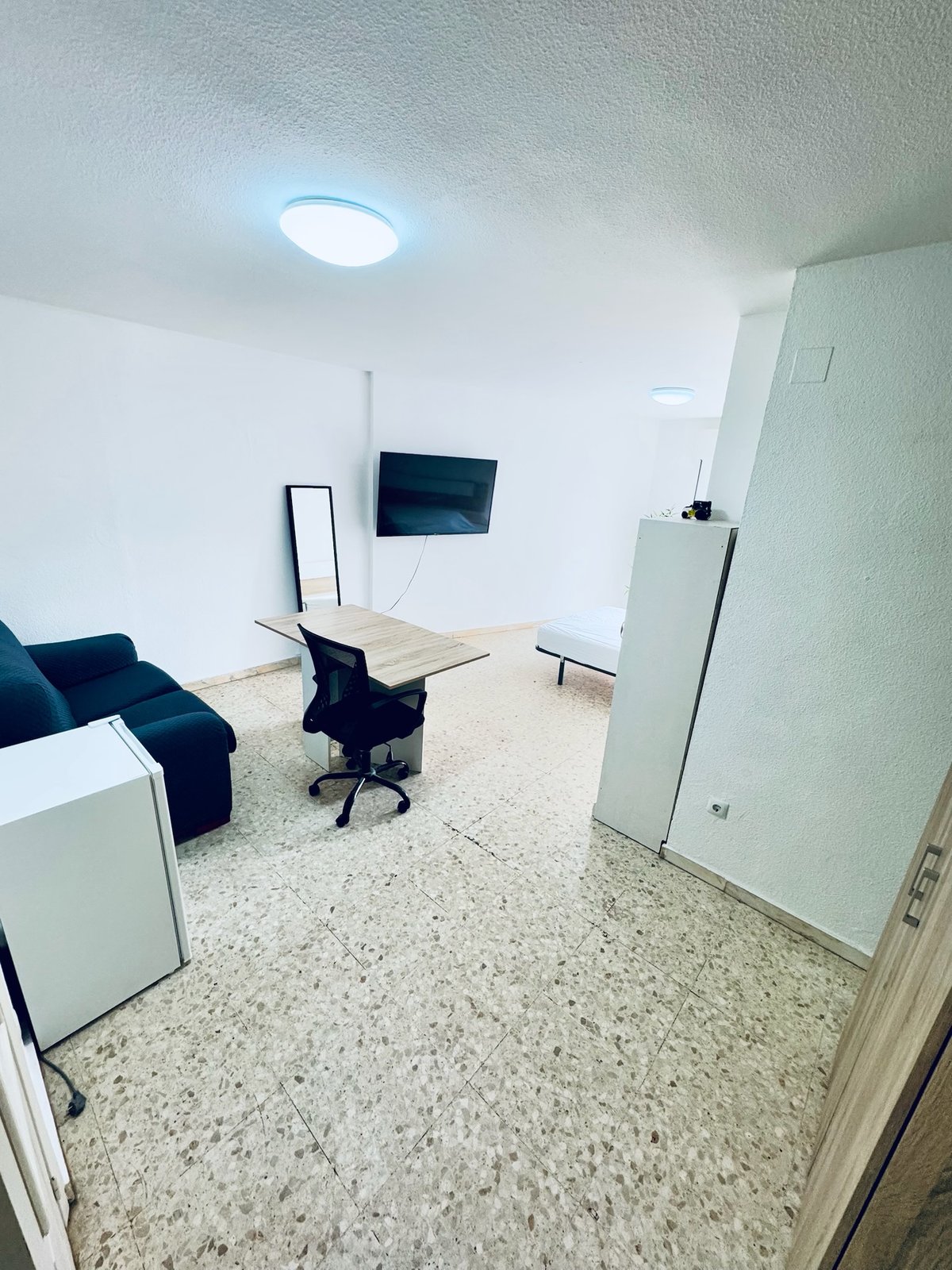 Habitación H42 · vista desde la entrada con sofá, TV, espejo y mini nevera